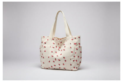 Beige tote bag with red floral pattern on a surface near a window.