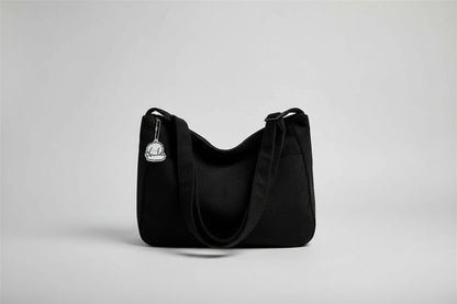 Black corduroy handbag with a keychain on a white surface near a window with blinds.