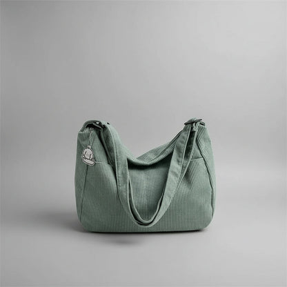 Green corduroy handbag on a white surface with blinds in the background