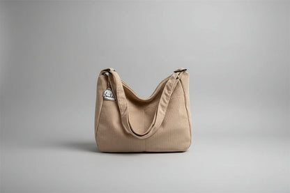 Beige corduroy handbag with a small white cat plushie on a surface with blinds in the background