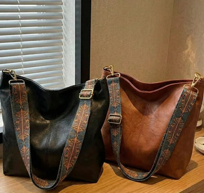 Two leather handbags, one black and one brown, with decorative straps on a wooden surface.